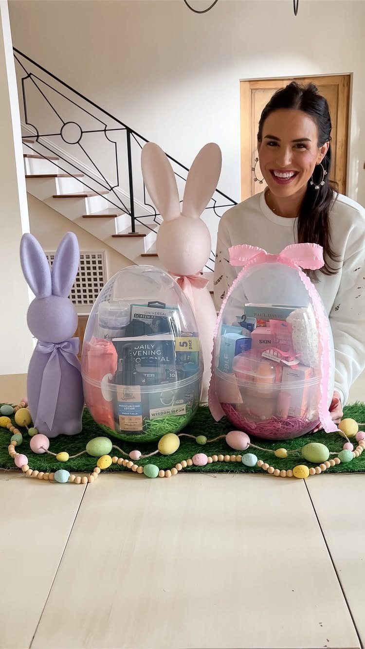 Woman posing with clear egg-shaped Easter baskets filled with gifts and bunny decorations.