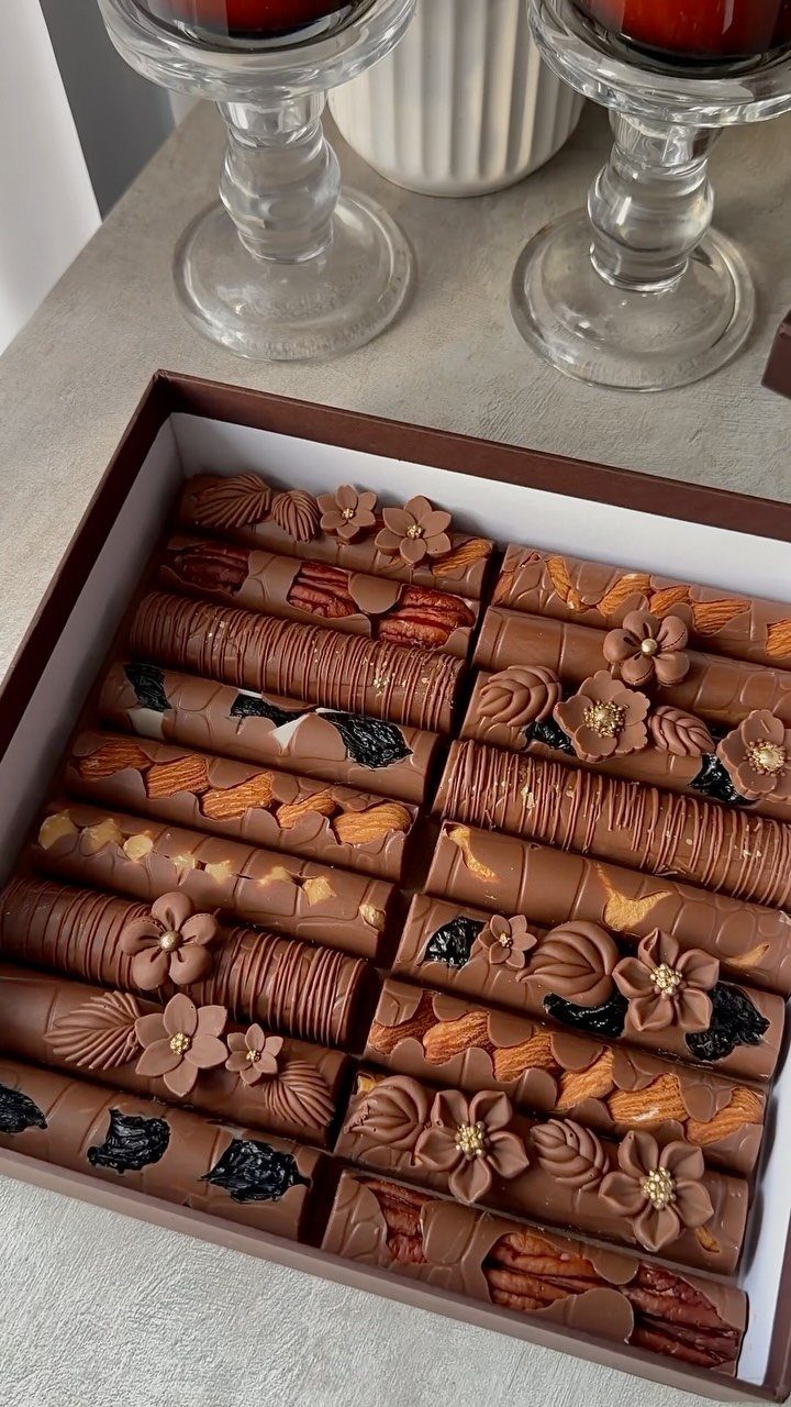 Assorted artisanal chocolate cylinders with floral decorations in a brown gift box.