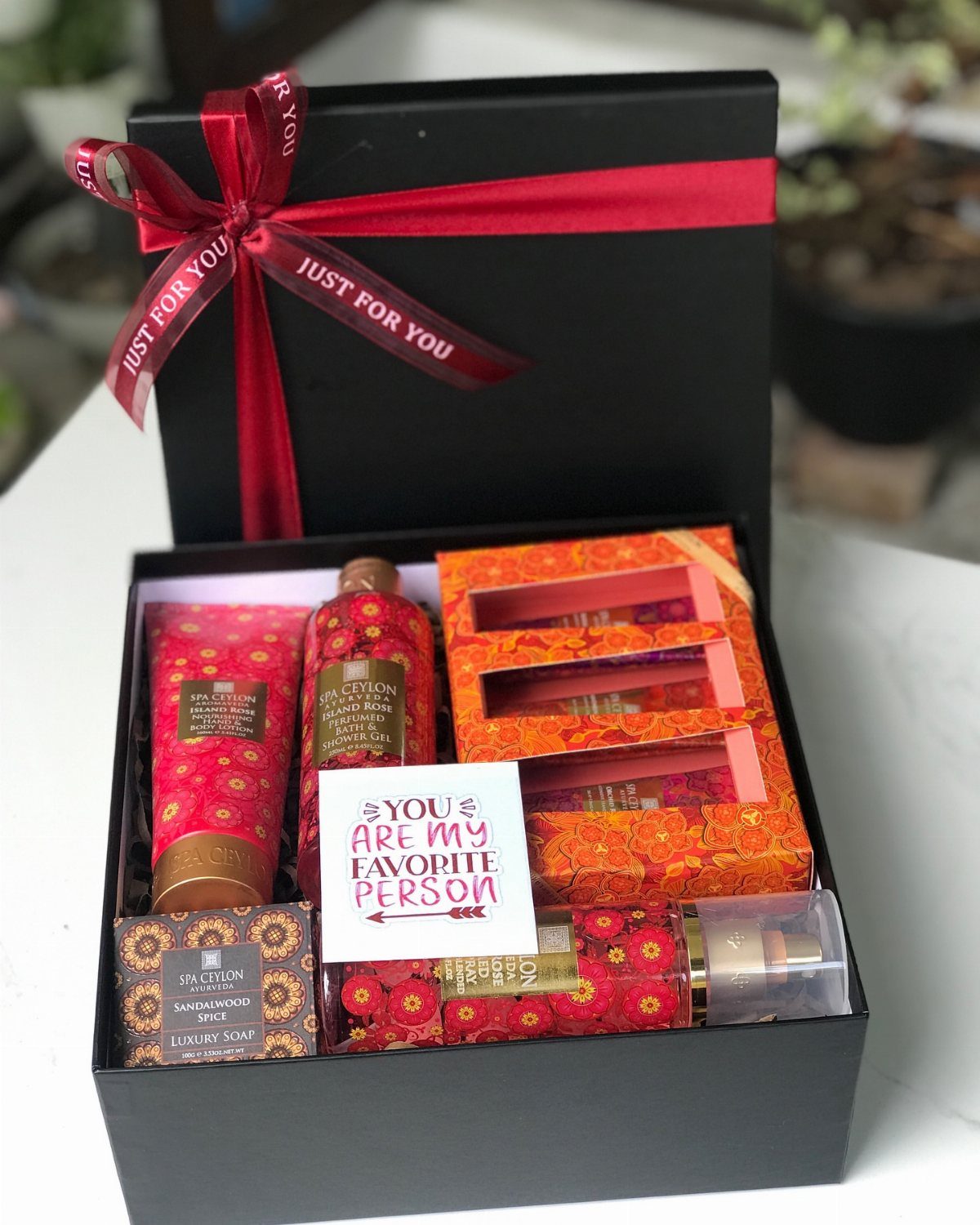 Black gift box with red ribbon containing red patterned luxury body care products.