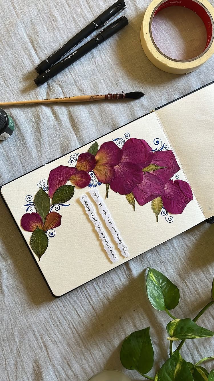 Open notebook with pressed purple flower petals and green leaves on a fabric surface.