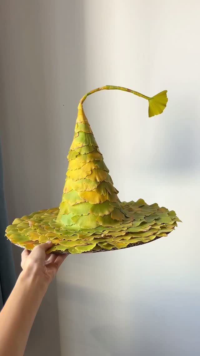 Pointed witch hat made of yellow and green leaves held by a hand