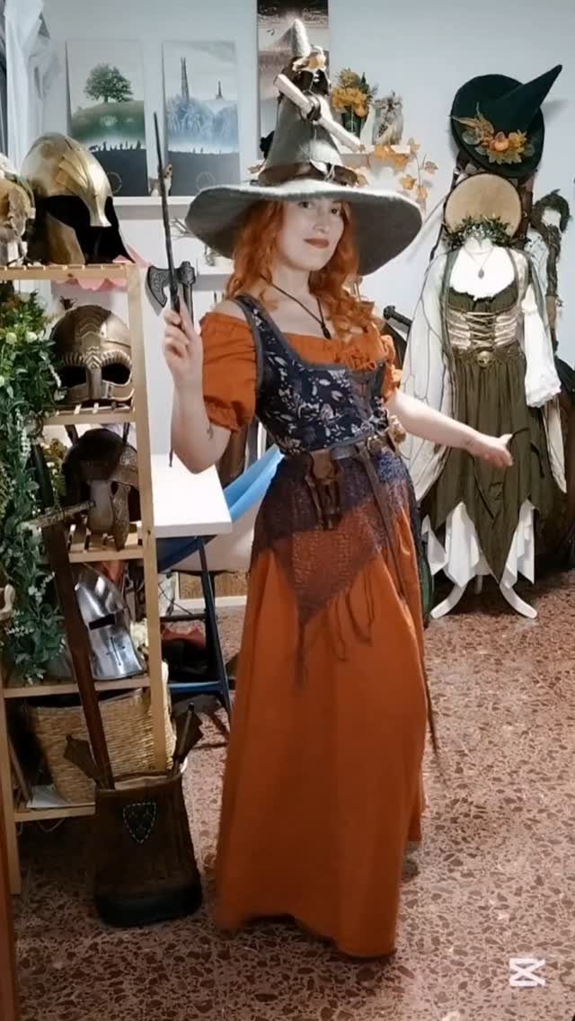 Woman in orange dress and grey witch hat holding a small axe