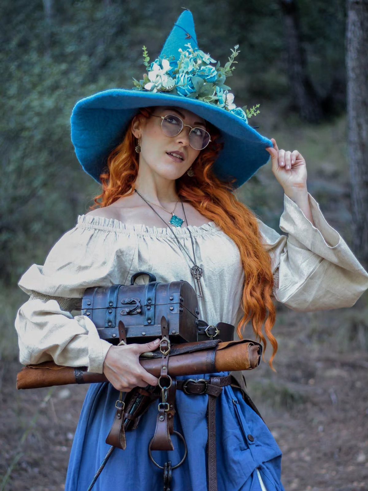 Woman with red hair wearing a blue witch hat and cream blouse in woods