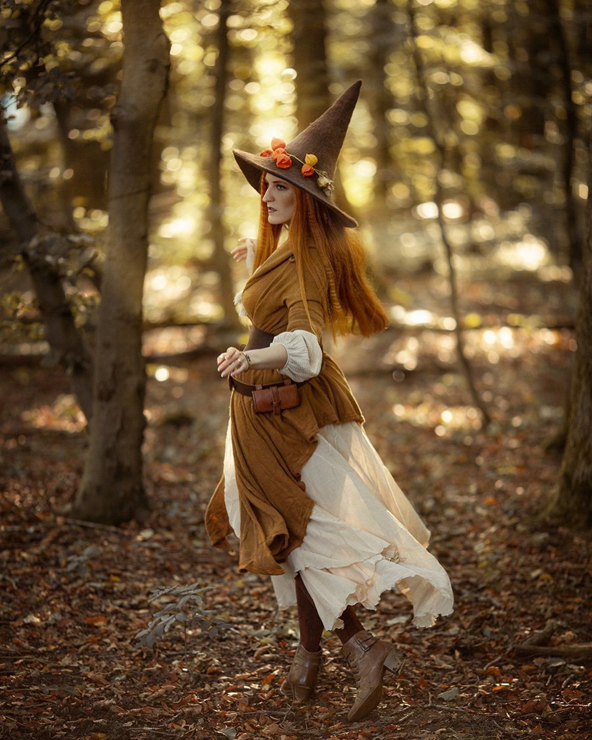 Woman in brown pointed witch hat and corset dress standing in autumn forest