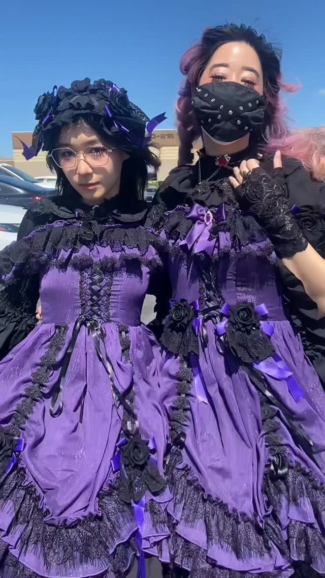 Two women wearing layered purple and black lace gothic dresses with ribbons.