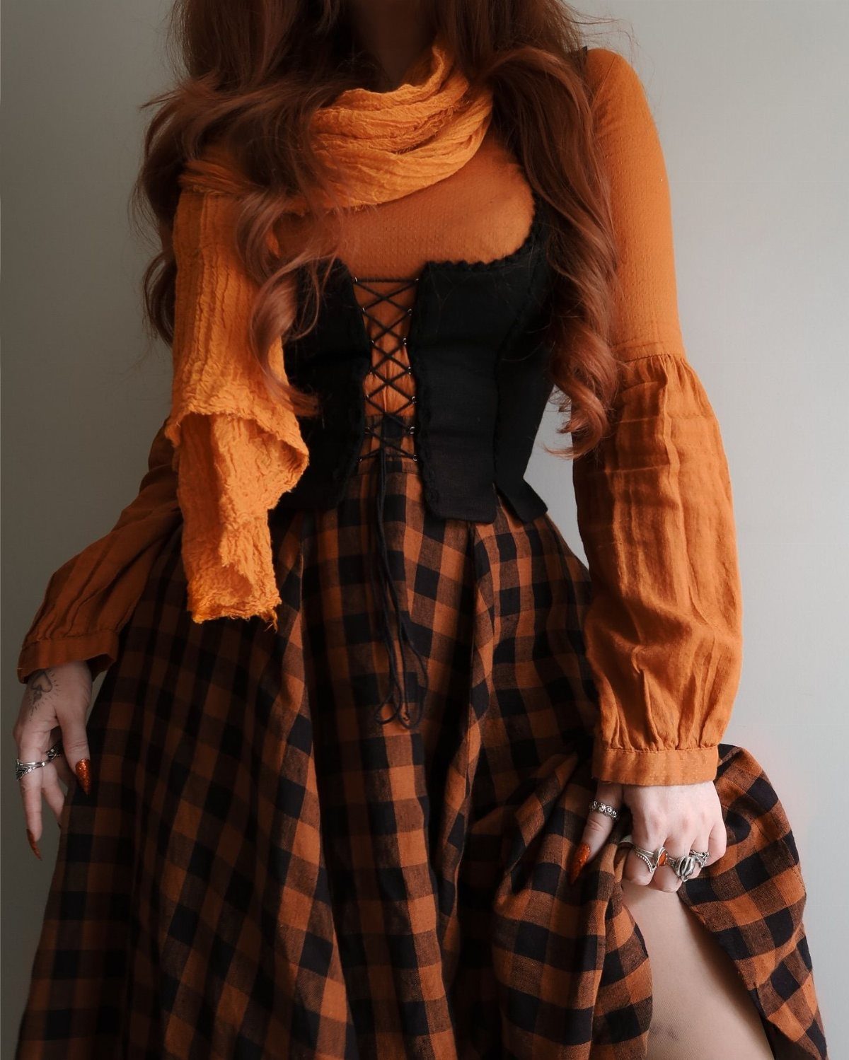 Person wearing orange top, black corset, and orange plaid skirt with orange scarf.