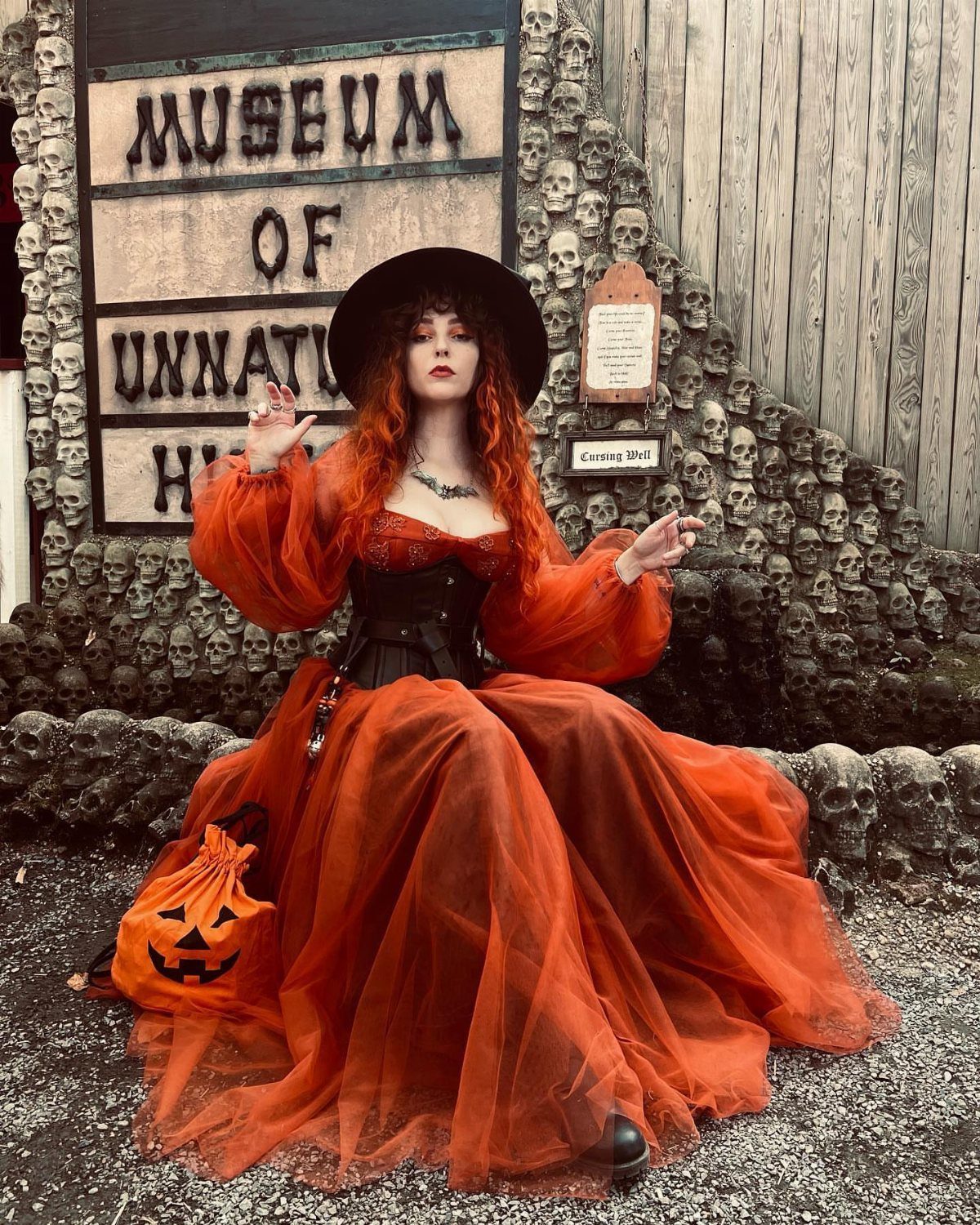 Woman in orange tulle dress and black hat posing by skull wall