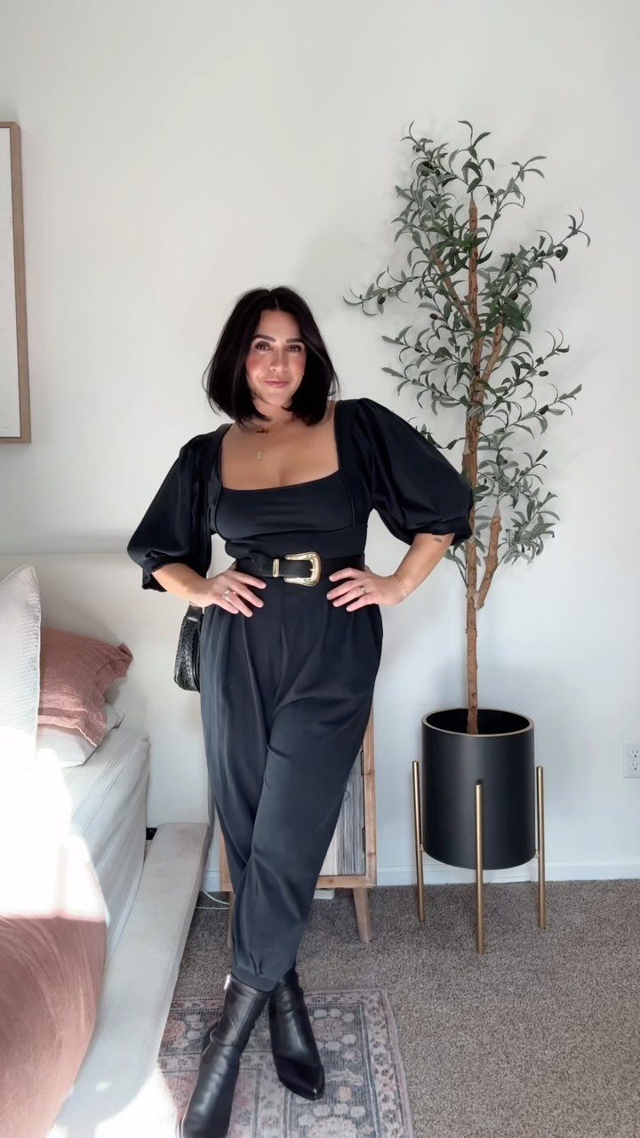 Woman wearing a black puff-sleeve jumpsuit with a belt and black boots.