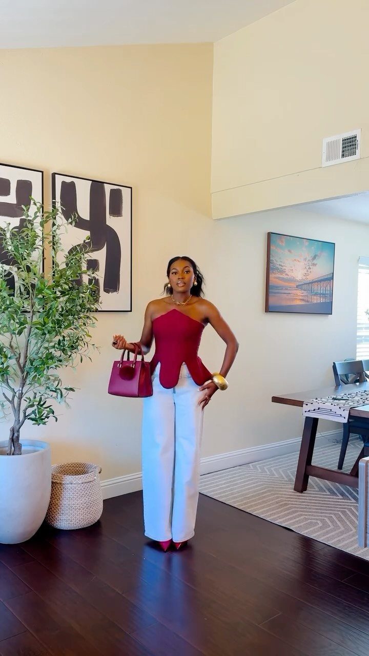 Woman wearing a burgundy corset top and white wide-leg trousers with matching handbag.