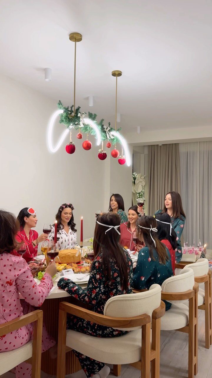 Women wearing colorful patterned pajama sets gathered around a festive holiday dinner table.