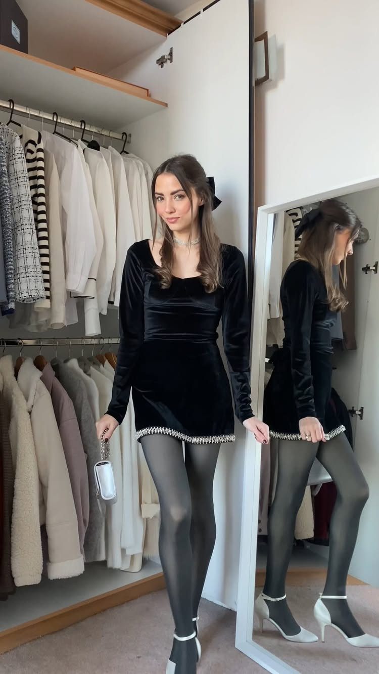 Woman in a short black velvet dress and white heels in a closet.