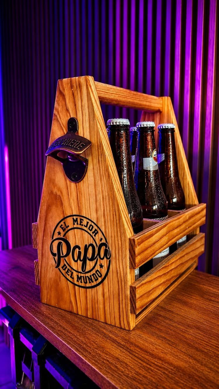 Wooden beer caddy holding brown bottles with a bottle opener and Spanish text.