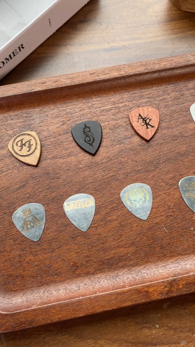 Various custom guitar picks made of wood and metal on a wooden tray.