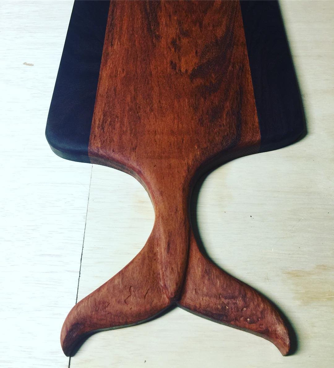 Fish tail shaped wooden cutting board with reddish-brown and dark wood tones.