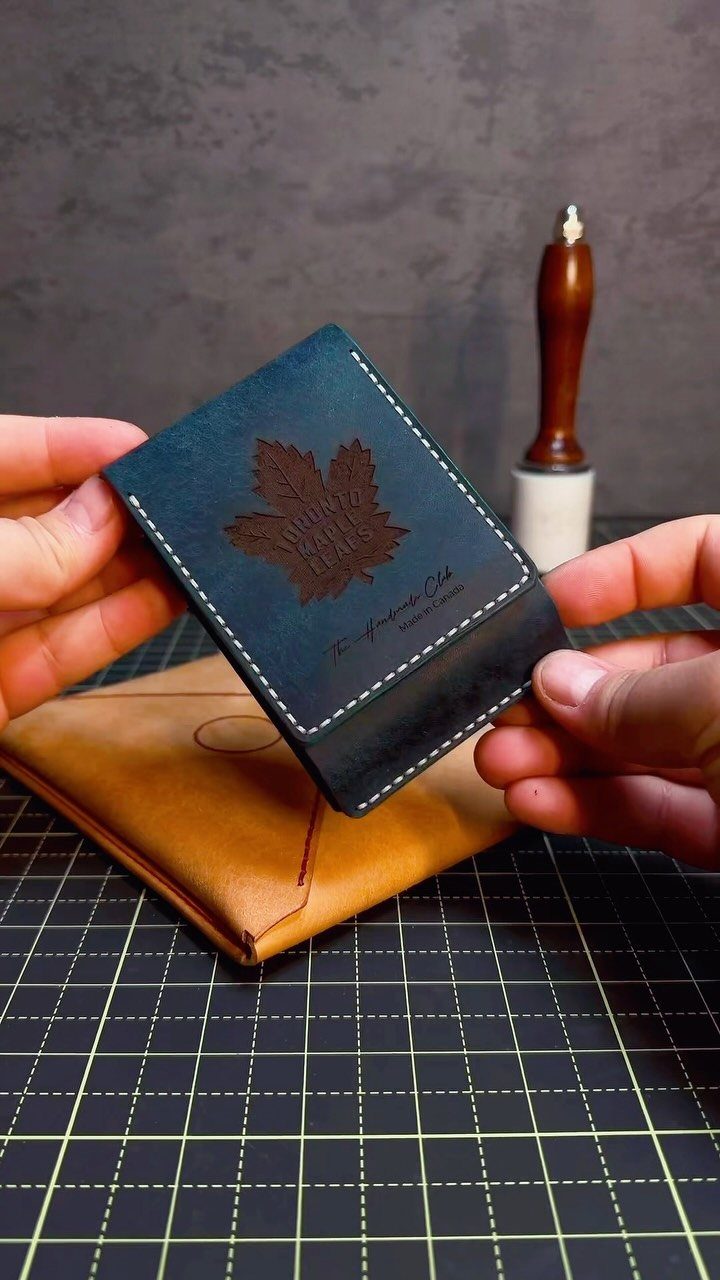 Blue leather wallet insert with a maple leaf design held over a tan wallet.