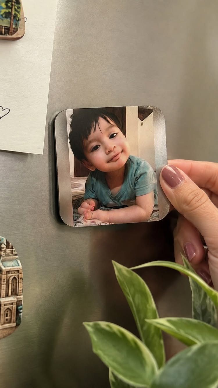 Small square photo magnet of a smiling child held against a refrigerator