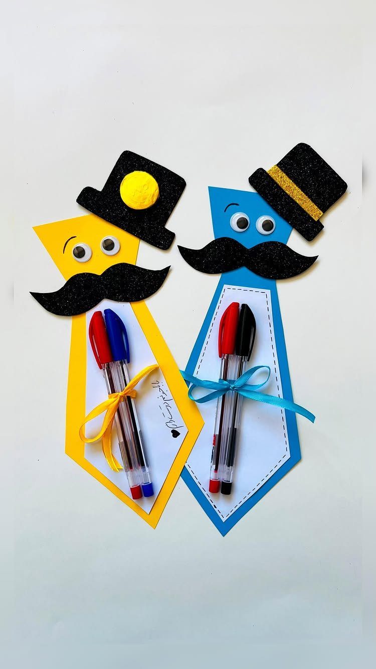 Two colorful tie-shaped cardstock crafts with mustaches and hats holding pens.