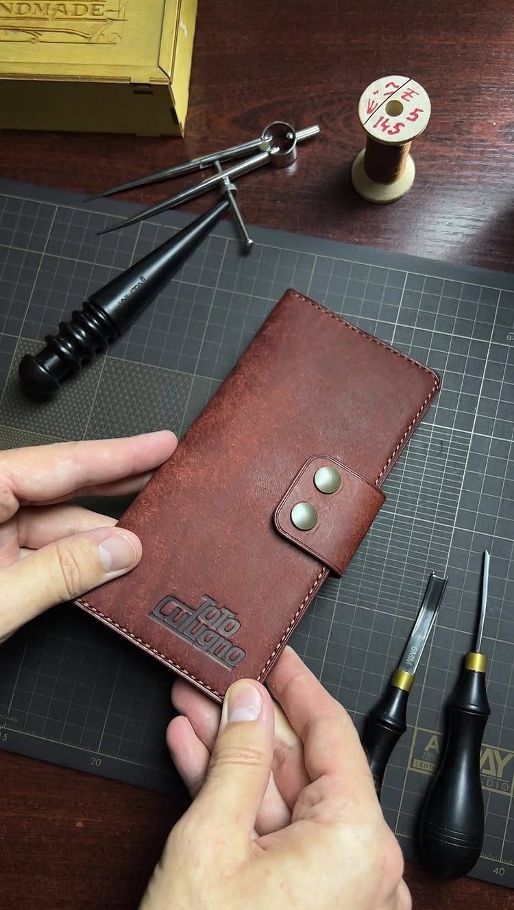 Handmade brown leather wallet held by hands on a leatherworking tool mat