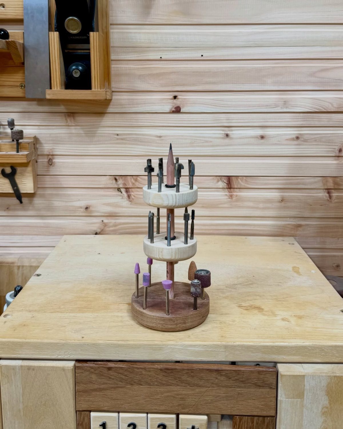 Three-tiered wooden tool holder with carving chisels on a light wood workbench