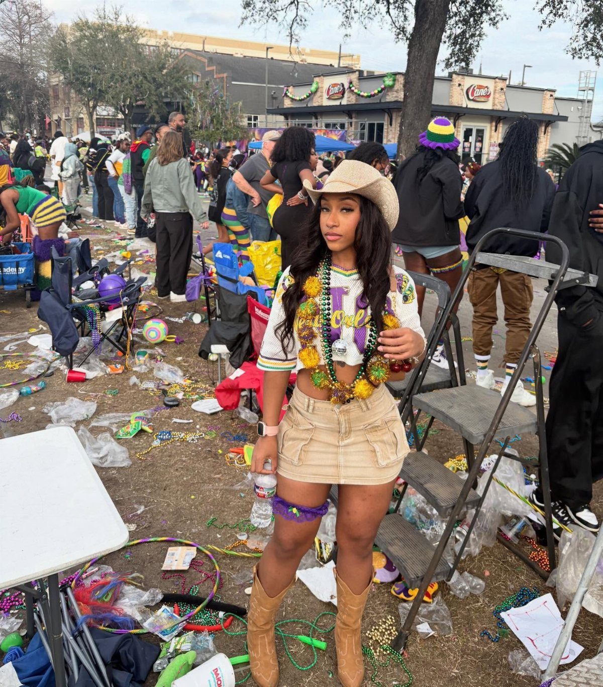 Woman wearing a cowboy hat, tan skirt, and colorful beads at Mardi Gras.
