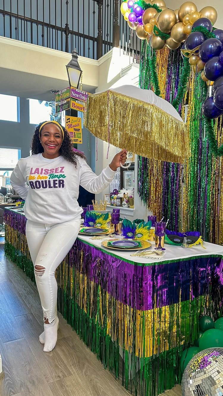 Woman in white Mardi Gras attire holding a gold umbrella by a decorated table