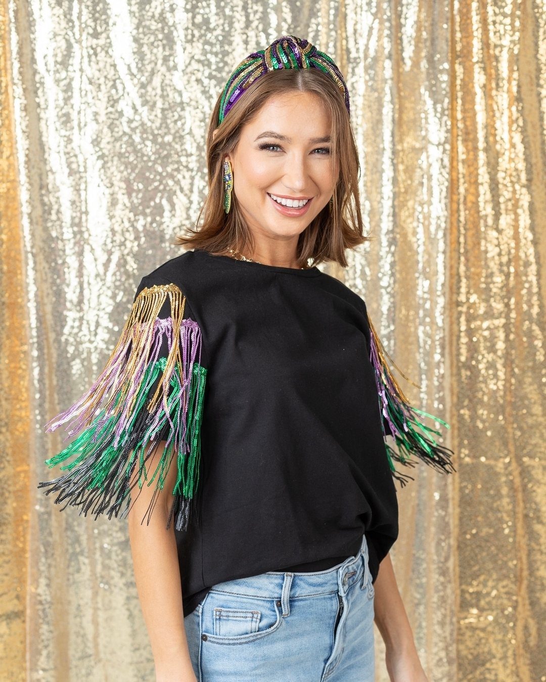 Woman in a black fringe top and beaded headband against gold sequins.