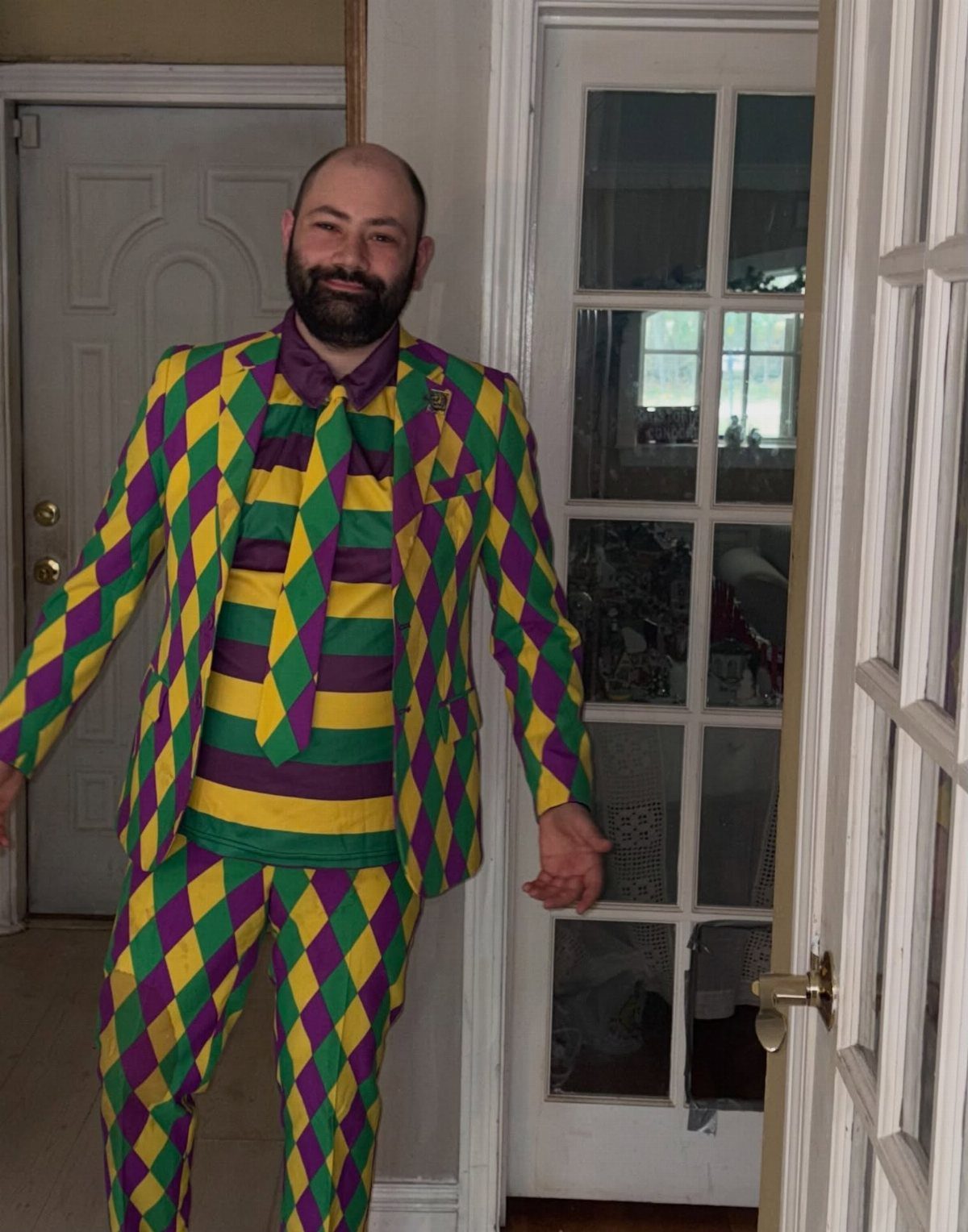 Man wearing a purple, green, and yellow diamond-patterned jester suit indoors.