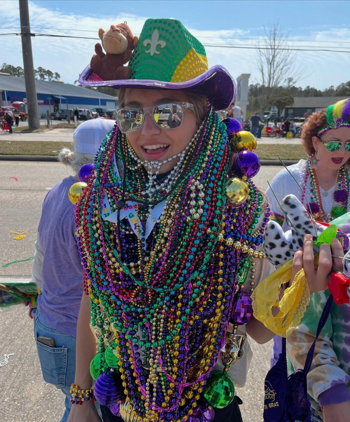 Woman wearing a festive hat and many layers of purple, green, and gold beads.