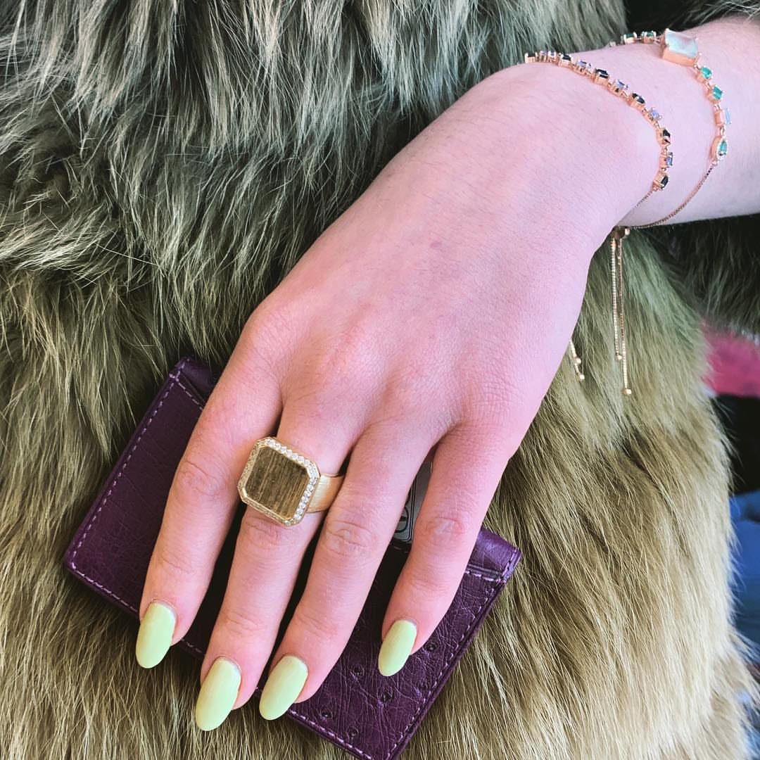 Hand with green nails and gold ring resting on a purple wallet.