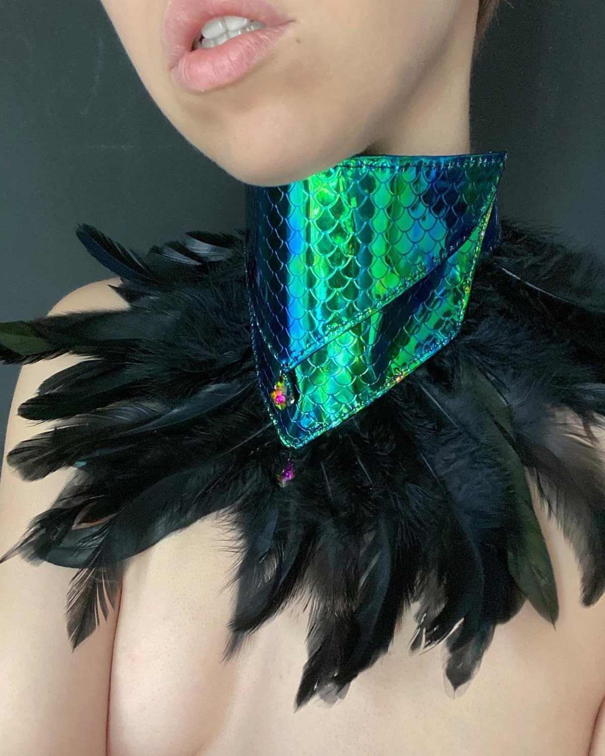 Iridescent green scale collar with black feathers worn around a person's neck.