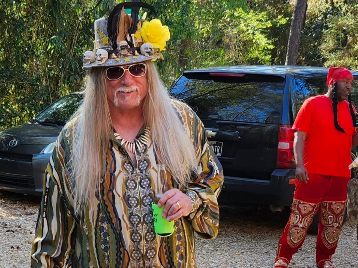 Man in colorful patterned shirt and skull-decorated top hat at a party.