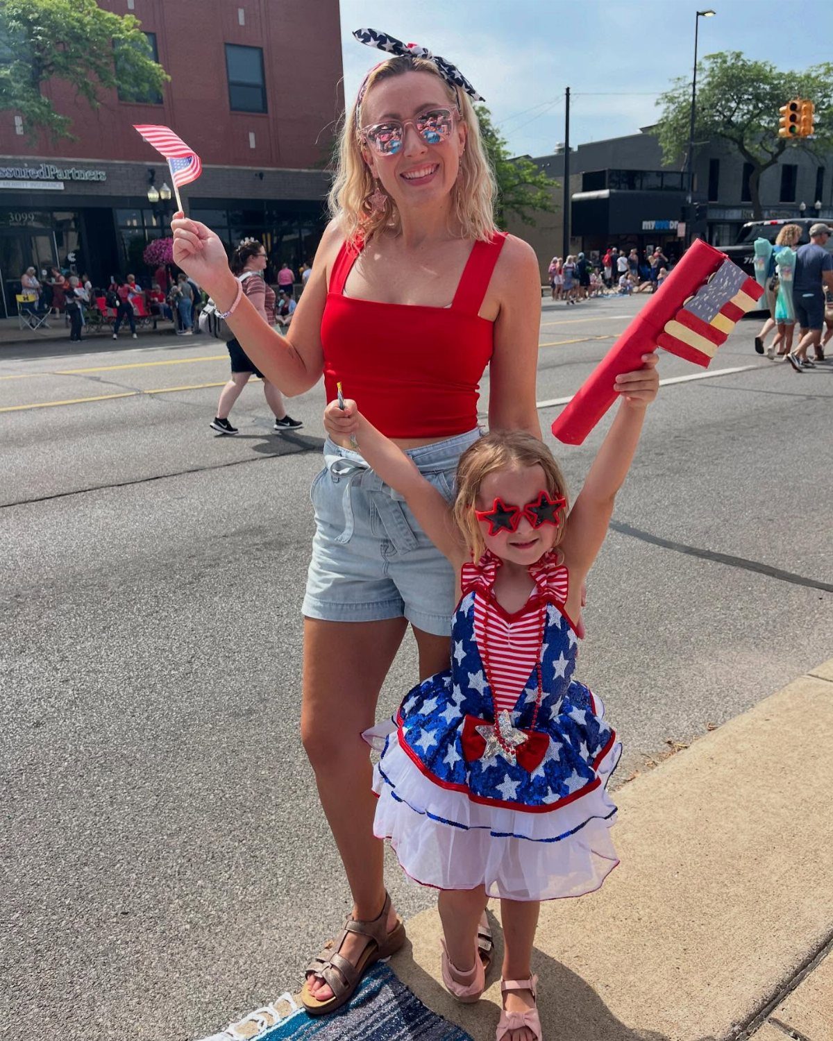 Woman in red top and denim shorts with girl in patriotic dress.