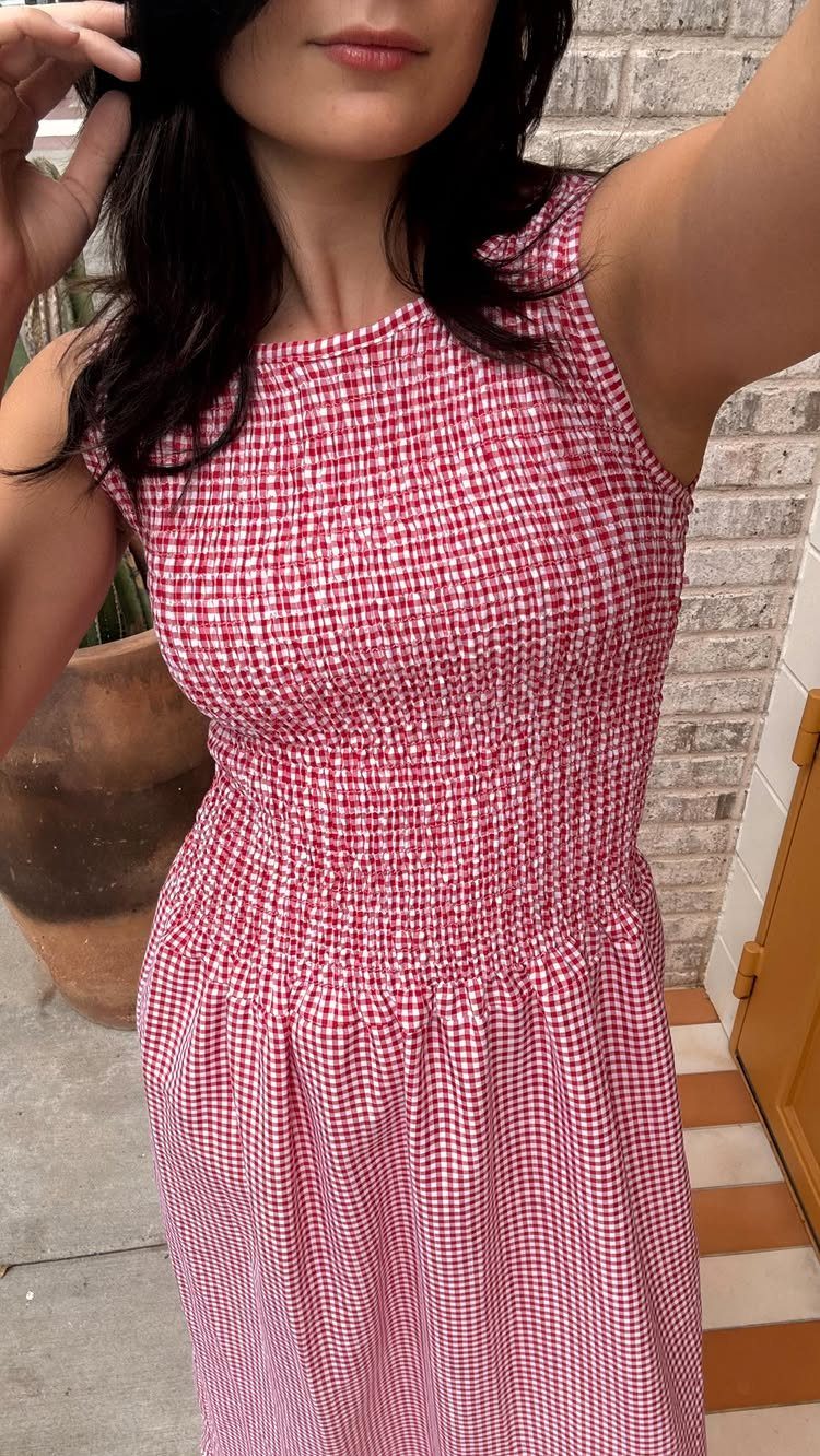 Woman wearing a red and white gingham smocked dress standing outdoors.