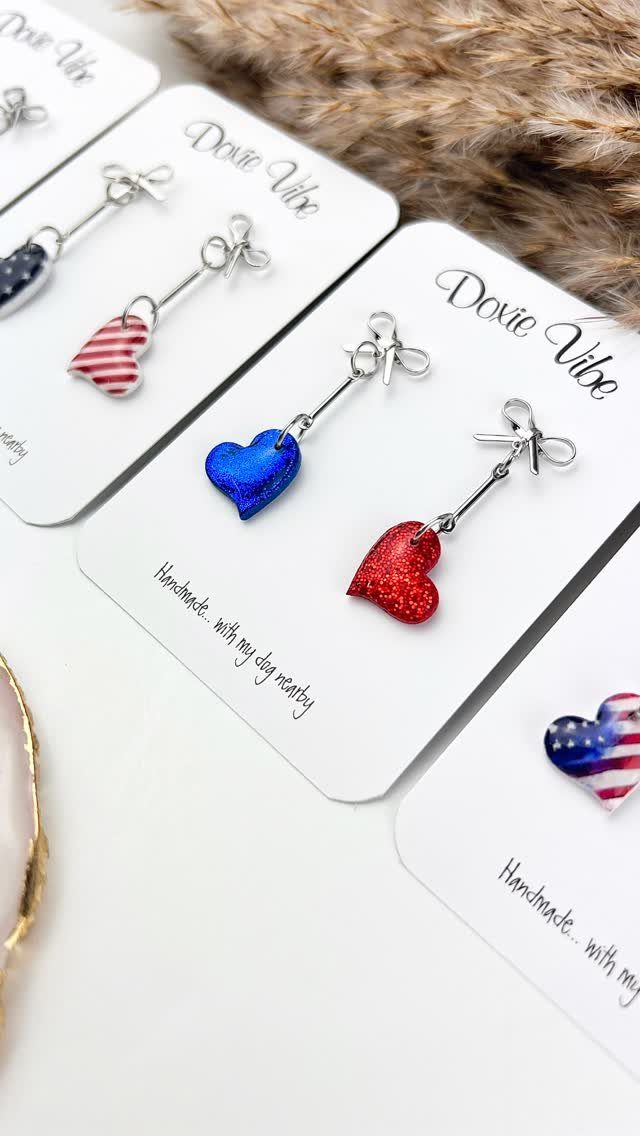 Heart-shaped patriotic earrings in red, blue, and flag patterns on white cards.