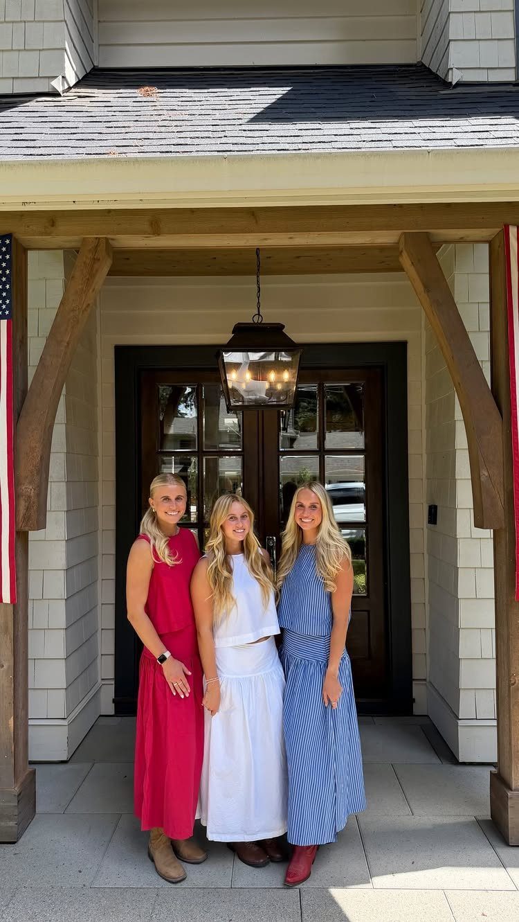 Three women posing in red, white, and blue dresses in front of a house.