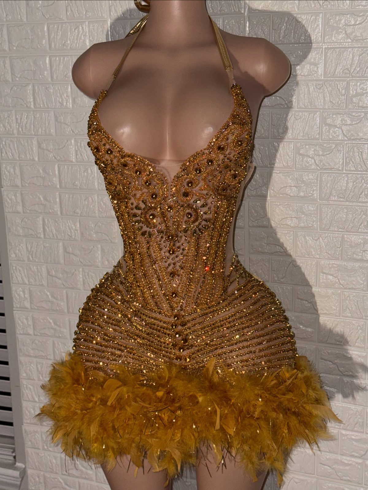 Gold beaded mini dress with yellow feather trim on a beige mannequin