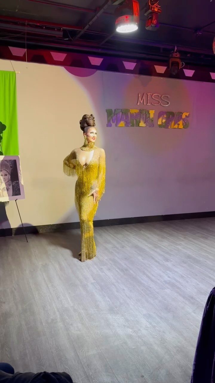 Woman in a gold floor-length fringed gown posing in front of a wall.