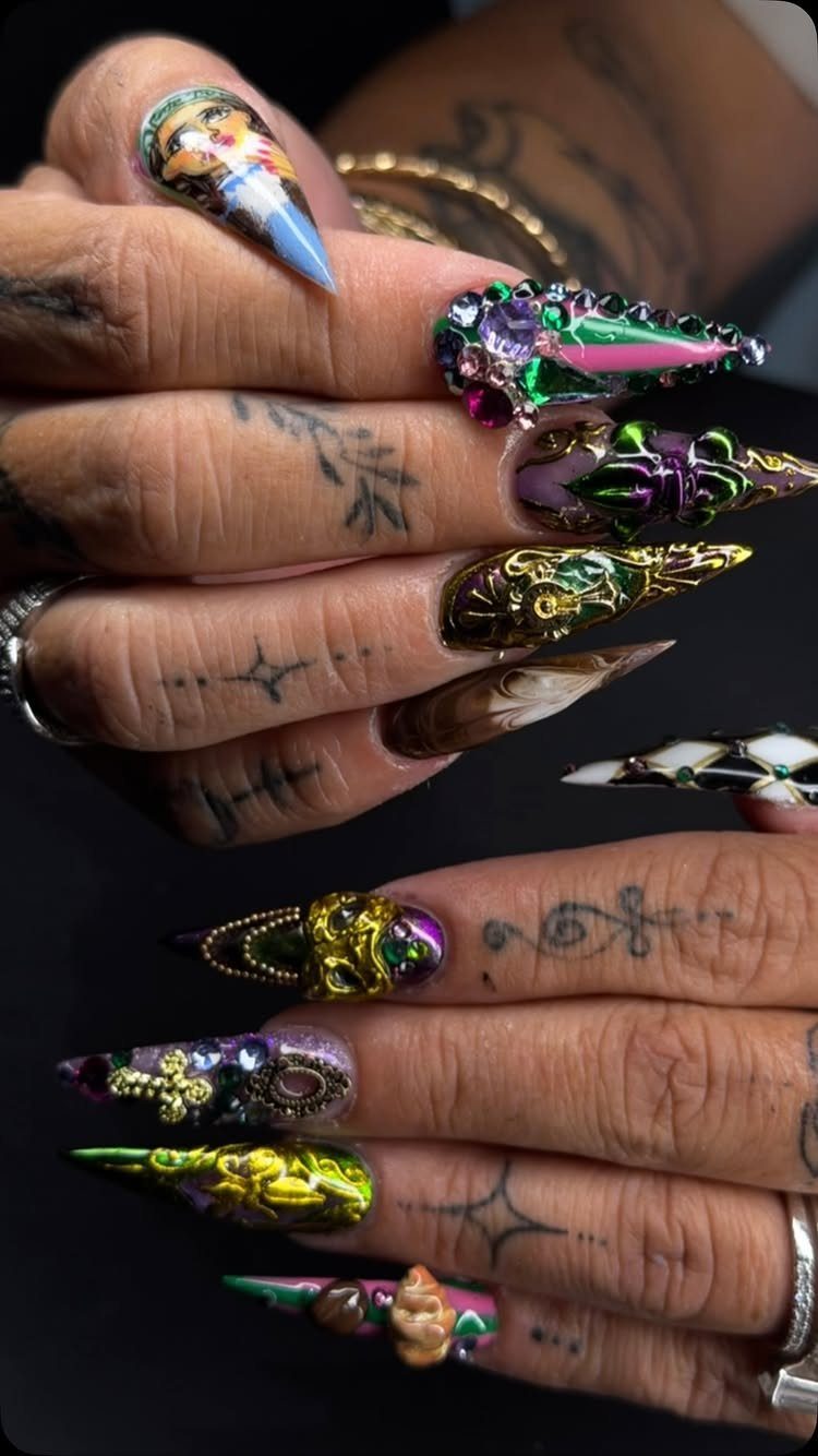 Stiletto nails with 3D gold and purple carnival designs and sparkling gemstones.