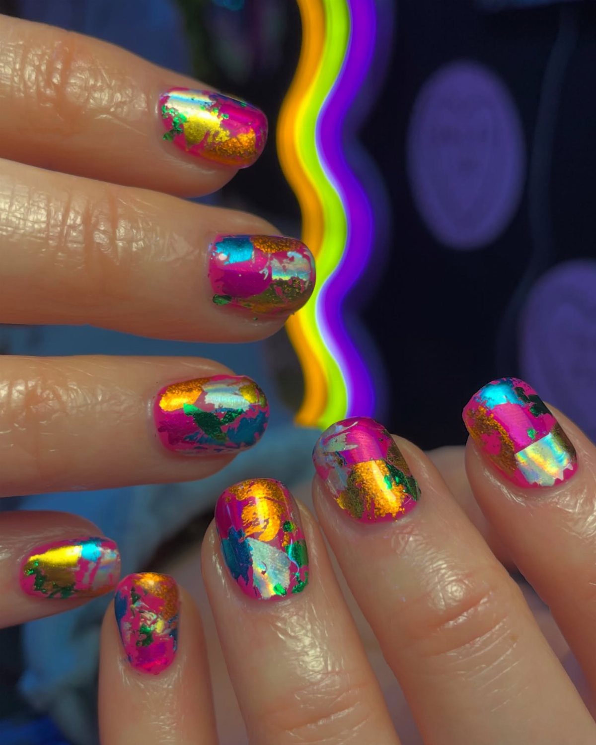 Fingernails decorated with iridescent purple, green, and gold metallic foil nail art.