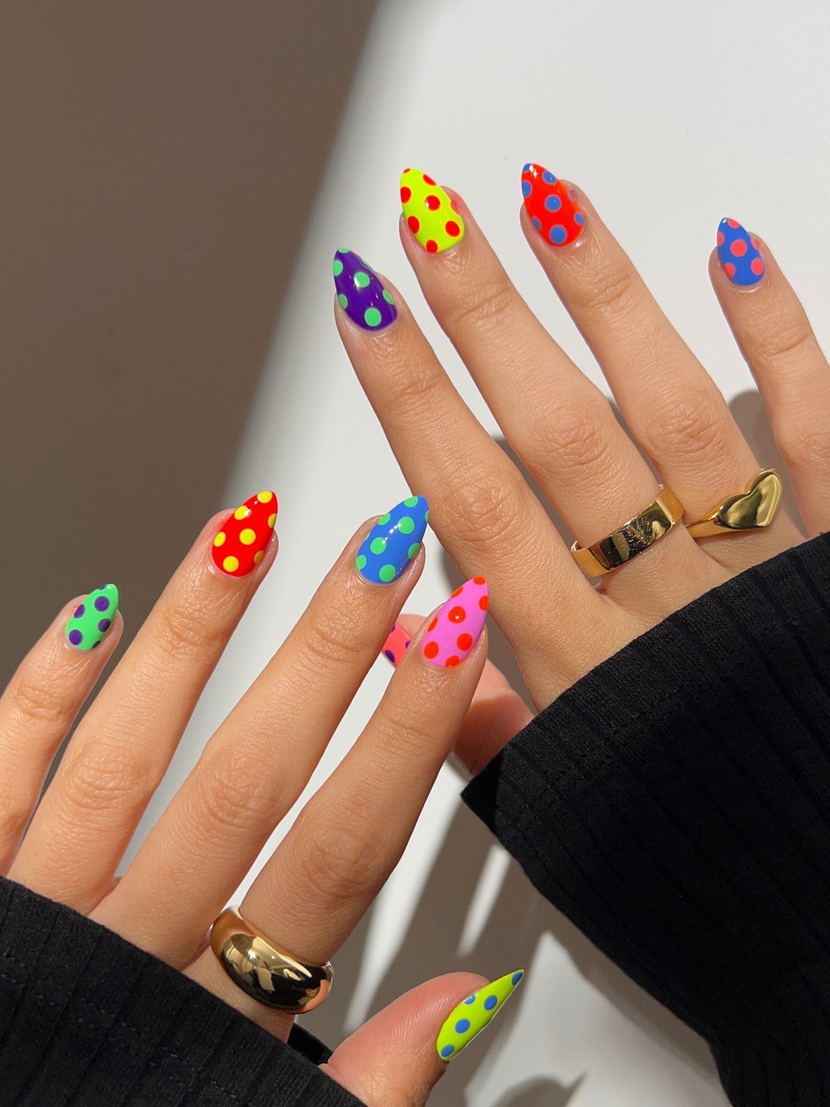 Colorful pointed nails with bright polka dots and gold rings on fingers.