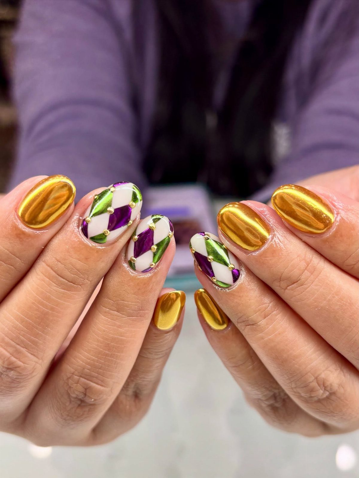 Manicured nails with metallic gold and purple, green, and white criss-cross patterns.
