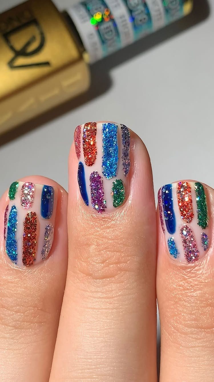 Fingernails with vertical glitter stripes in purple, green, gold, and blue colors.