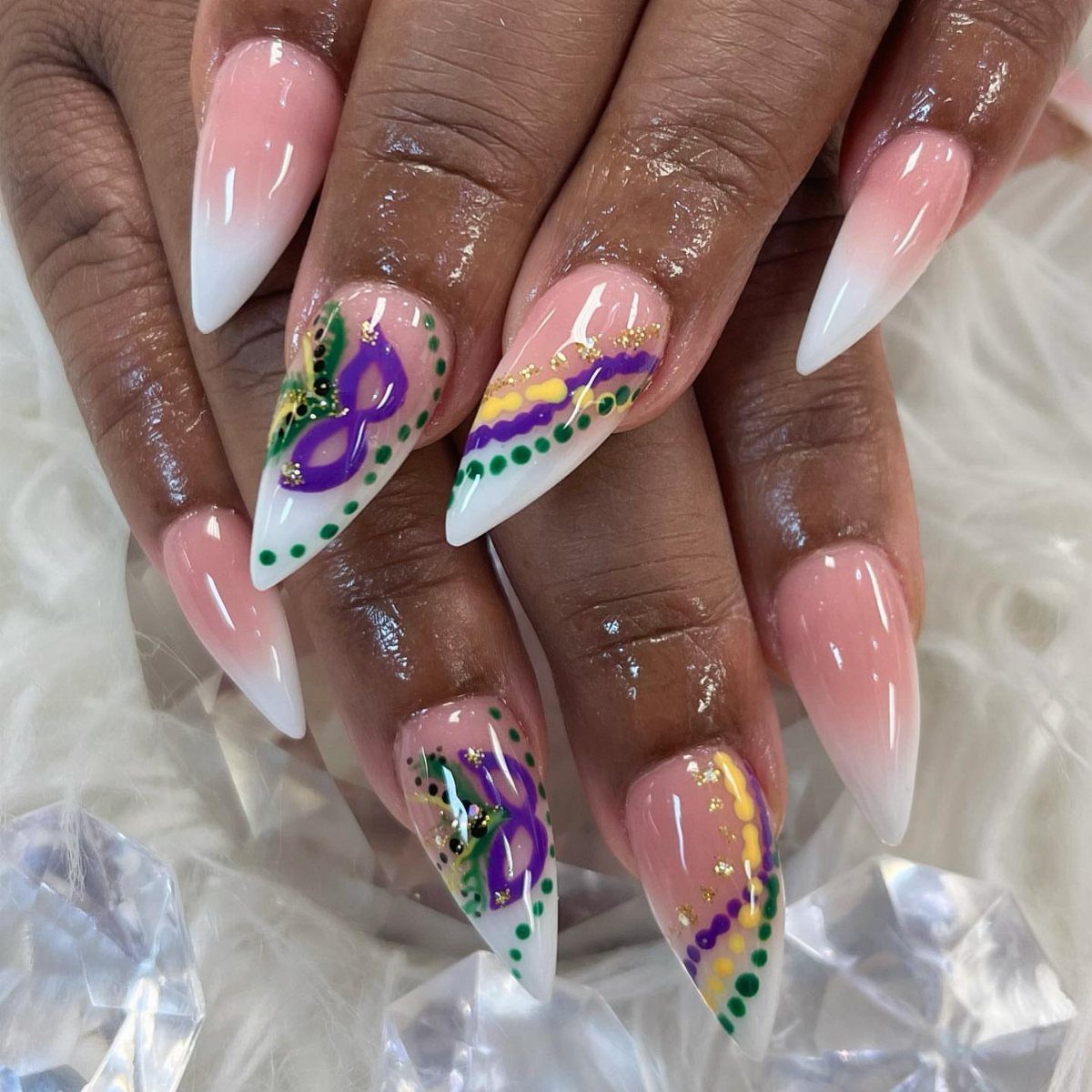 Almond-shaped nails with purple, green, and gold Mardi Gras mask nail art designs.
