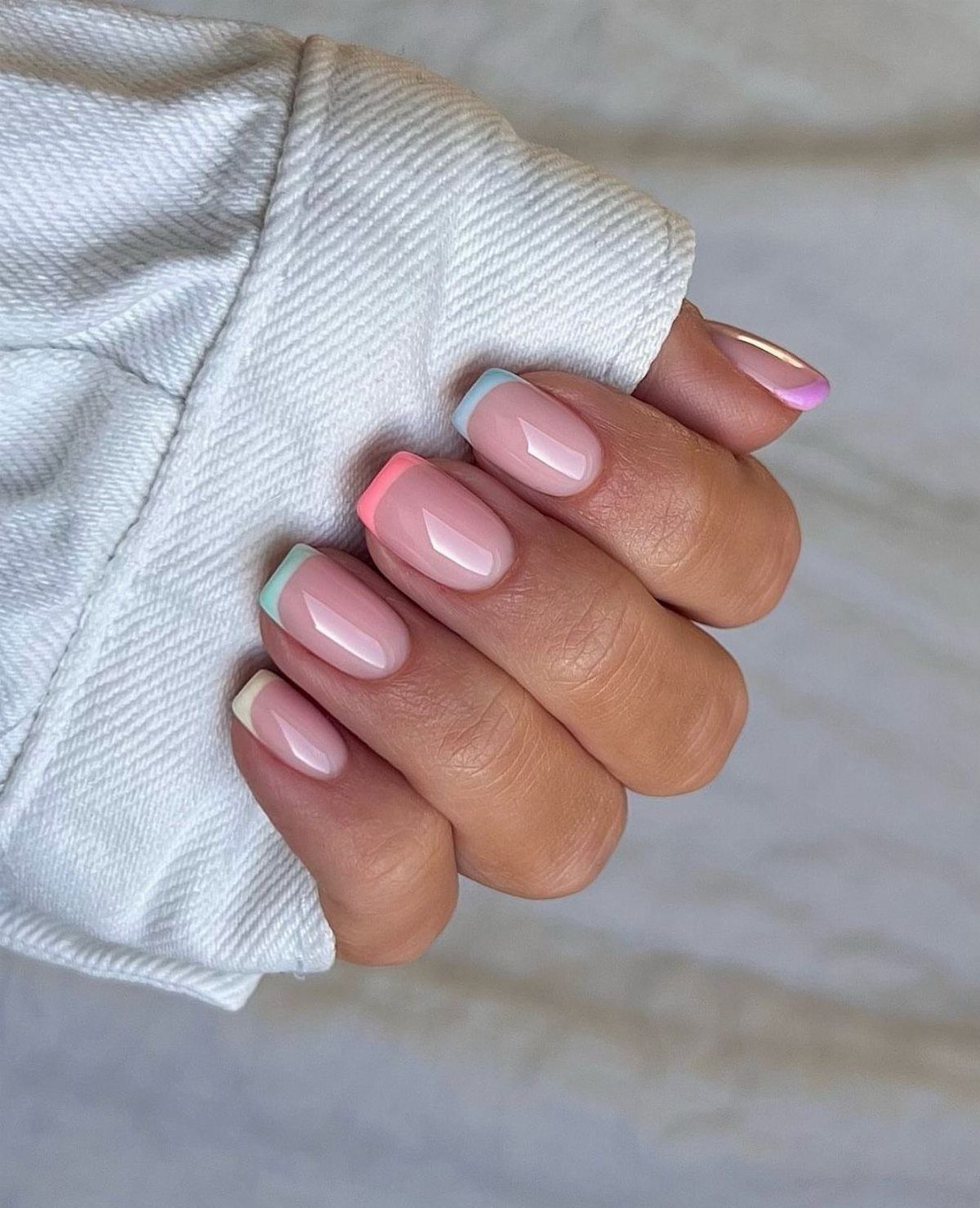 Hand with French manicure featuring purple, pink, green, and gold colored nail tips.