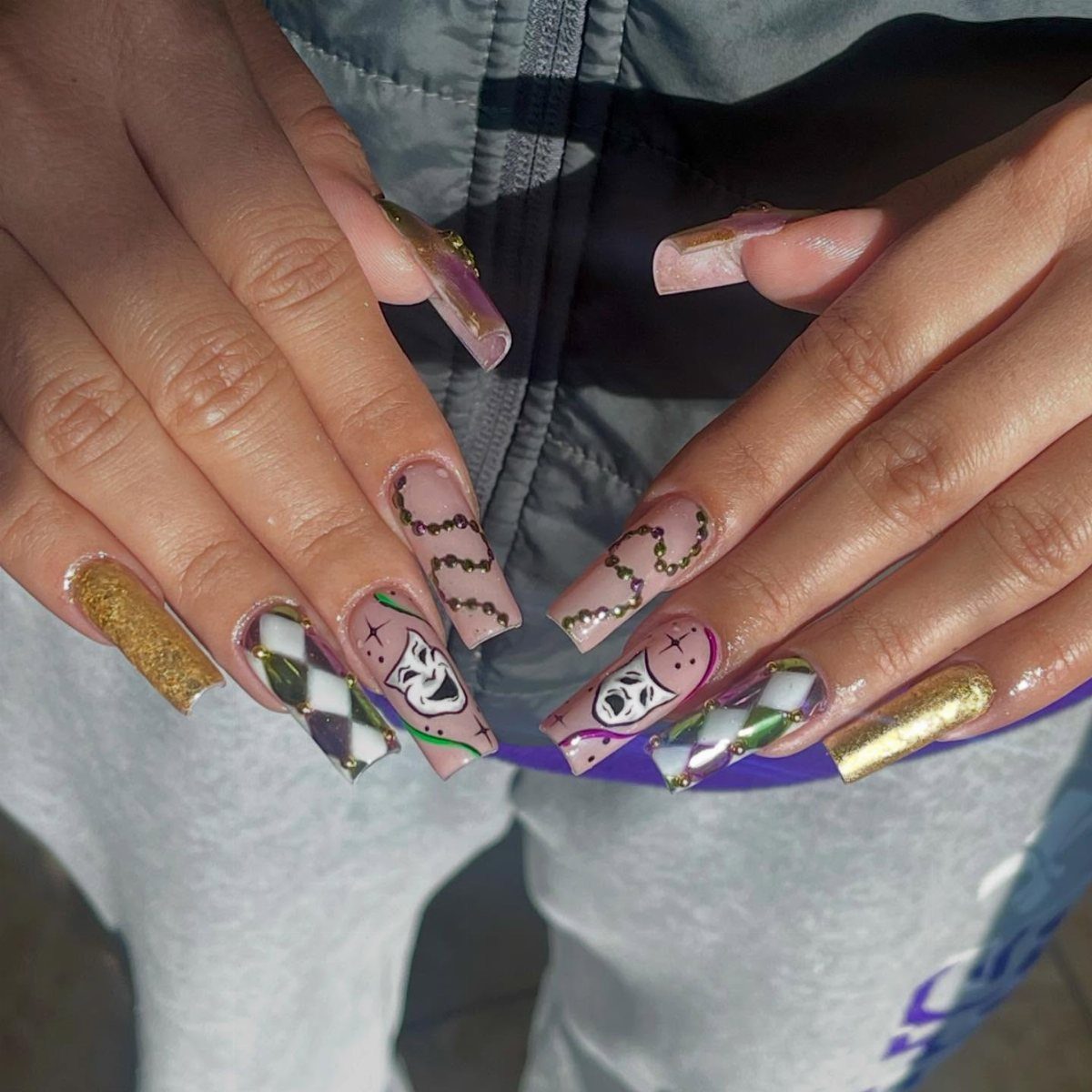 Long coffin nails with purple, gold, and green art featuring tiny painted masks.