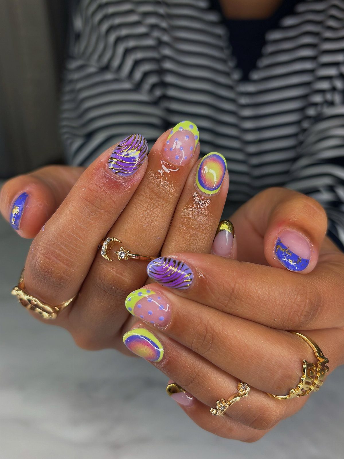 Manicured nails with purple, gold, and green swirls and glitter on a hand.