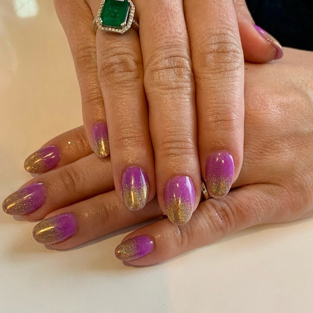 Purple nails with gold glitter ombre tips and a large emerald ring.