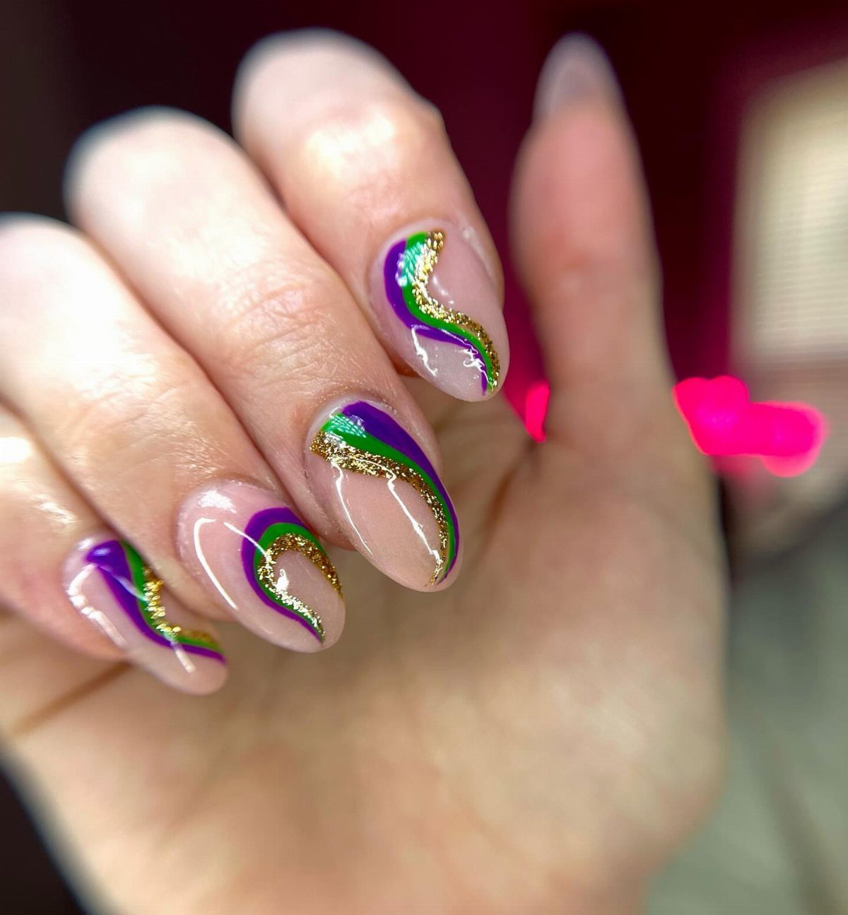 Almond-shaped nails with purple, green, and gold glitter swirls on a clear base.