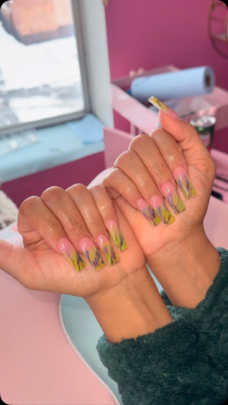 Hands with long coffin nails featuring purple, green, and gold marbled art.