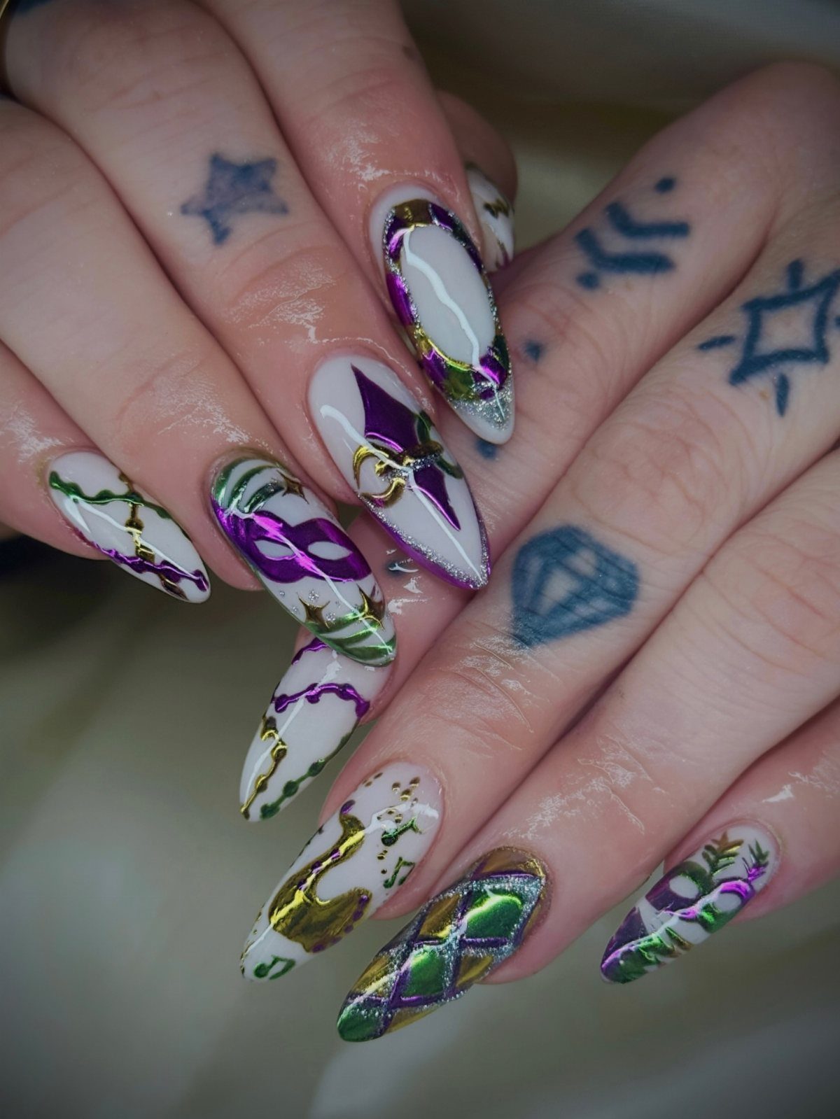 Almond-shaped nails with white, purple, green, and gold Mardi Gras inspired nail art.